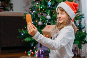 Ein Kind in Weihnachtsmannmütze zeigt Santa in einem Live-Videoanruf ein Geschenk.