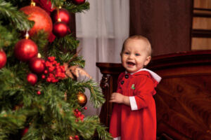 Ein Baby lacht vor Freude über eine Videobotschaft vom Weihnachtsmann, die vor dem Weihnachtsbaum abgespielt wird.