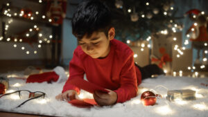Ein Kind liegt vor dem beleuchteten Weihnachtsbaum und betrachtet einen Brief vom Weihnachtsmann.
